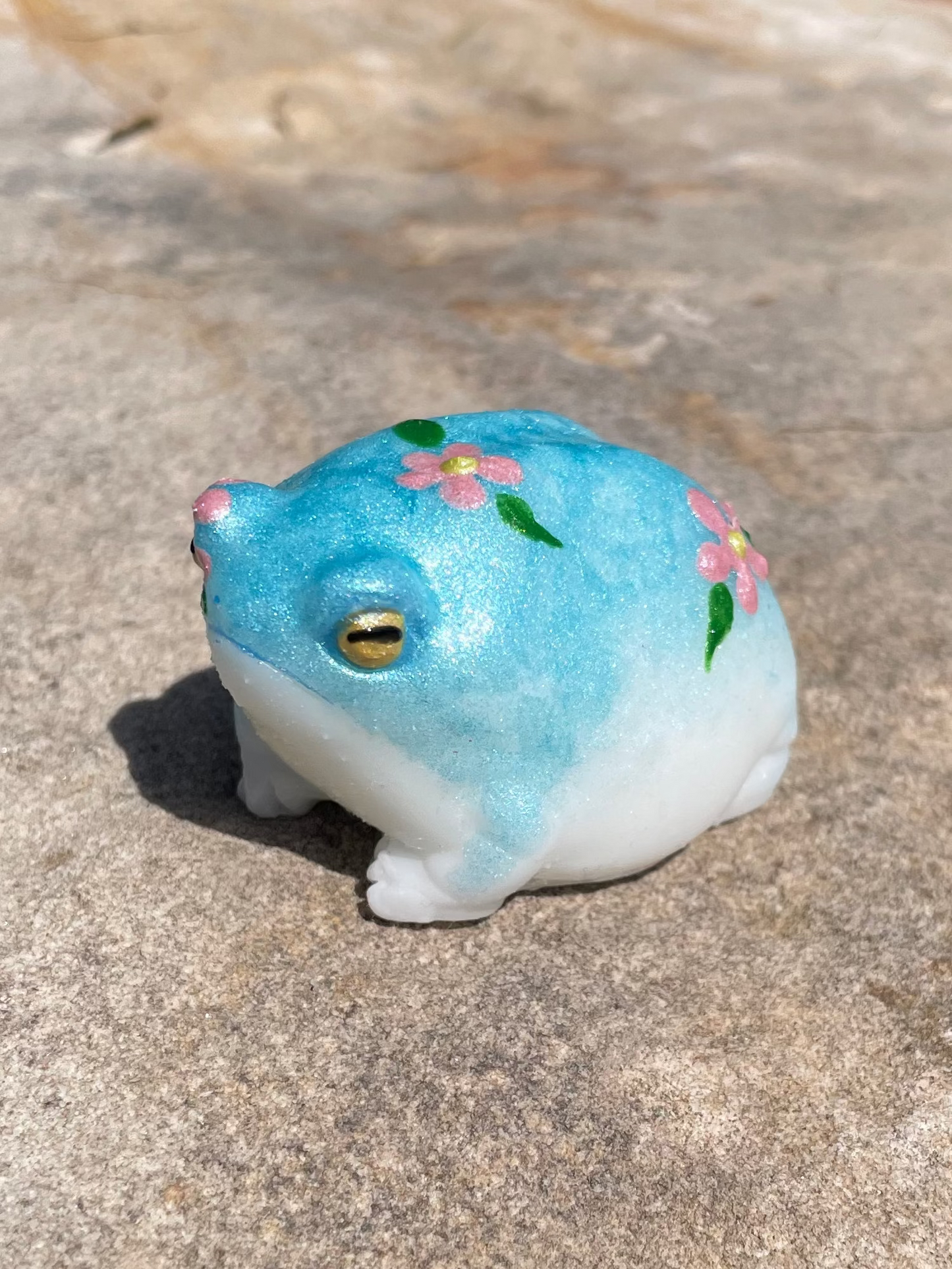 Blue frog with painted flowers sitting on a rock in the sun